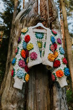 a crocheted sweater hanging from a tree in the woods with flowers on it