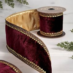 two rolls of red velvet ribbon with gold beading on them and evergreen branches in the background