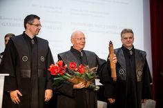 three men standing in front of a projector screen with flowers and an award on it