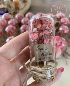 a hand holding a glass jar filled with tiny pink flowers and twine around it