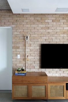 a flat screen tv sitting on top of a wooden cabinet in front of a brick wall