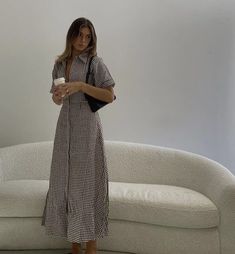 a woman standing in front of a white couch holding a cup and looking at the camera