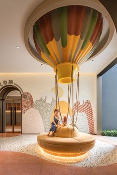 a child sitting on a swing in the middle of a room with large balloons hanging from the ceiling