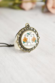 a small pendant with an image of a cat on it's side and flowers in the background