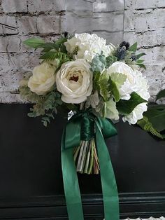 a bouquet of white flowers and greenery tied to a black box with a green ribbon