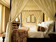 a canopy bed with white drapes and pillows on it's headboard in a bedroom