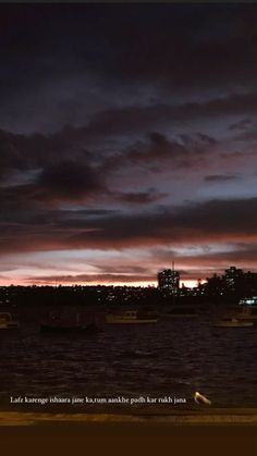 the sky is very dark and cloudy at night, with boats in the water below