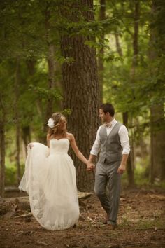 a bride and groom holding hands in the woods