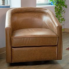 a brown leather chair sitting on top of a hard wood floor next to a potted plant