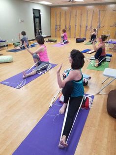 a group of people sitting on yoga mats in a gym doing stretching exercises with ropes