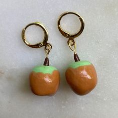 two orange and green apples are hanging from gold - plated hooks on a white surface