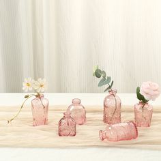 pink glass bottles with flowers in them on a table