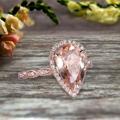 a pink diamond ring sitting on top of a wooden table next to some yellow flowers