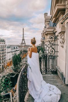 a woman in a wedding dress standing on a balcony looking at the eiffel tower