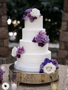 a wedding cake with purple and white flowers on the top is sitting on a table