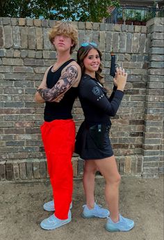 two people standing next to each other in front of a brick wall with tattoos on their arms