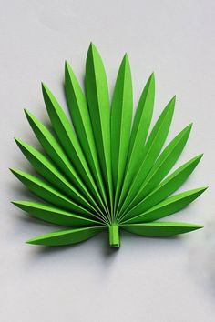 a green paper palm leaf sitting on top of a white table next to a clock