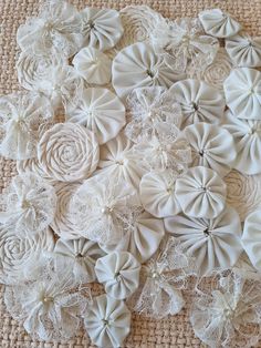 white fabric flowers are arranged on a table cloth with lace and pearls in the center