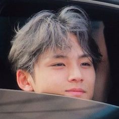 a young boy with grey hair looking out the window of a car while sitting in front of him