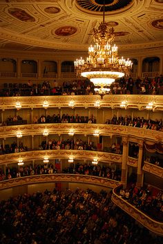 an auditorium filled with people and chandeliers in the middle of it's ceiling