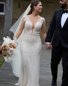 a bride and groom holding hands walking down the street in their wedding gowns,