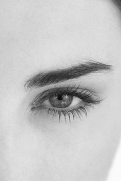 a woman's eye with long eyelashes and dark hair is shown in black and white