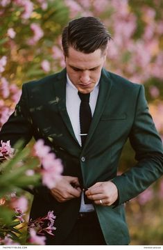 a man in a suit and tie standing next to pink flowers with his hands on his chest