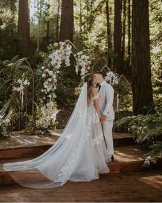 a bride and groom kissing in front of an arch with white flowers on the side