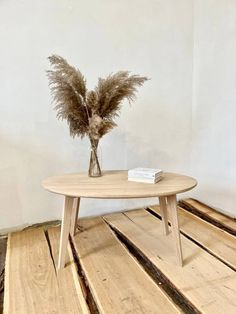 a wooden table with a vase on it and some dried grass in the middle, against a white wall