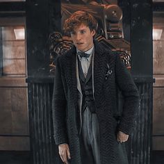 a man in a suit and bow tie standing next to a table with a clock on it