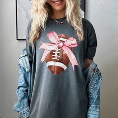 Step up your game day style with the Football Coquette Bow Comfort Colors Graphic Tee! This short sleeve tee combines a playful bow design with football flair, perfect for showing off your team spirit with a touch of chic. Made from ultra-soft Comfort Colors fabric, this tee ensures maximum comfort and a relaxed fit, making it an ideal choice for cheering from the stands or tailgating. Proudly made in the USA, it’s designed to be a standout piece in your game day wardrobe. Details:This listing i Sporty T-shirt For Game Day In Spring, School Spirit T-shirt For Game Day In Spring, Sports Fan Tops For Game Day In Spring, Spring Cheerleading Crew Neck T-shirt, Casual Tops For Game Day During Football Season, Fall Team Spirit Short Sleeve T-shirt, Team Spirit Short Sleeve T-shirt For Fall, Casual T-shirt For Cheerleading During Baseball Season, Casual Crew Neck T-shirt For Cheerleading