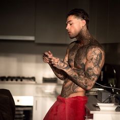 a man with tattoos standing in a kitchen