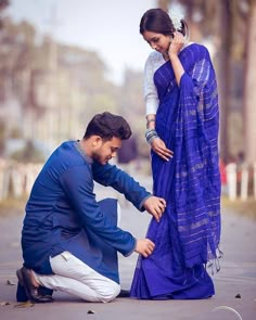 a man kneeling down next to a woman in a blue sari on the street