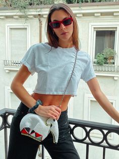 a woman wearing sunglasses and holding a purse standing on a balcony with her hands in her pockets