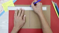 two hands on a piece of cardboard with pencils and paper tape next to them