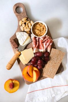 a wooden cutting board topped with cheese, meats and fruit next to crackers