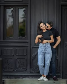 a man and woman standing next to each other in front of a black door hugging