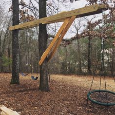 a wooden swing set in the woods with hammocks hanging from it's sides