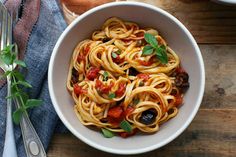 a white bowl filled with pasta and sauce on top of a wooden table next to silverware