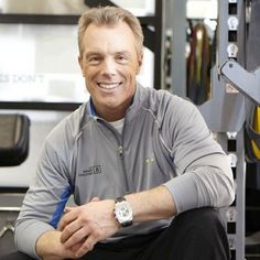 a man sitting on top of a bench in front of a gym equipment rack smiling at the camera