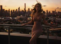 a woman standing on top of a balcony next to a railing with the city skyline in the background