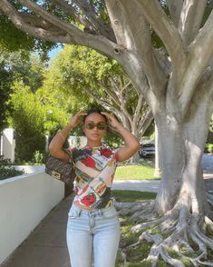 a woman standing next to a tree with her hand on her head and wearing sunglasses