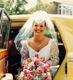 a bride sitting in the back of a yellow car with her bouquet and veil over her head