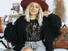 a woman sitting on a couch wearing a black shirt with a skeleton print and fringe sleeves