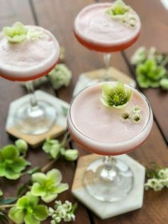 three glasses filled with different types of drinks on top of a wooden table next to flowers