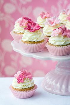 cupcakes with white frosting and pink flowers are on a cake platter