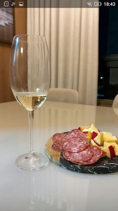 a glass of wine sitting next to a plate with meat and cheese on top of it