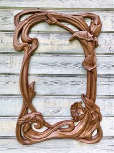 an ornate wooden frame with vines and leaves on it, against a white wood wall