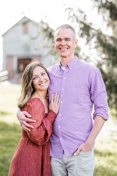 a man and woman standing next to each other in front of a tree with their arms around each other