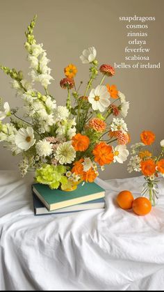 an arrangement of flowers and oranges on a bed